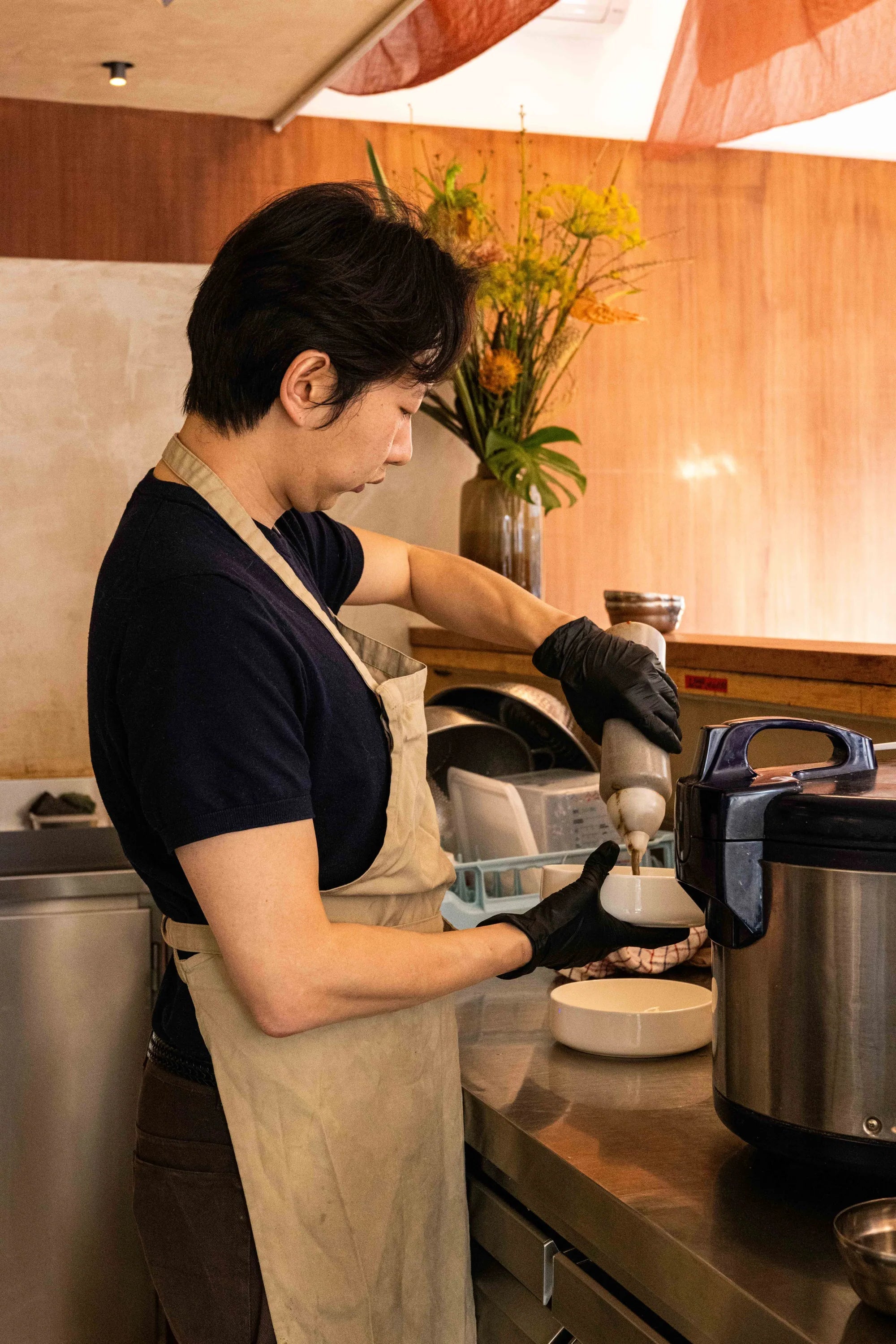 Person in a kitchen wearing an apron and gloves, preparing food.