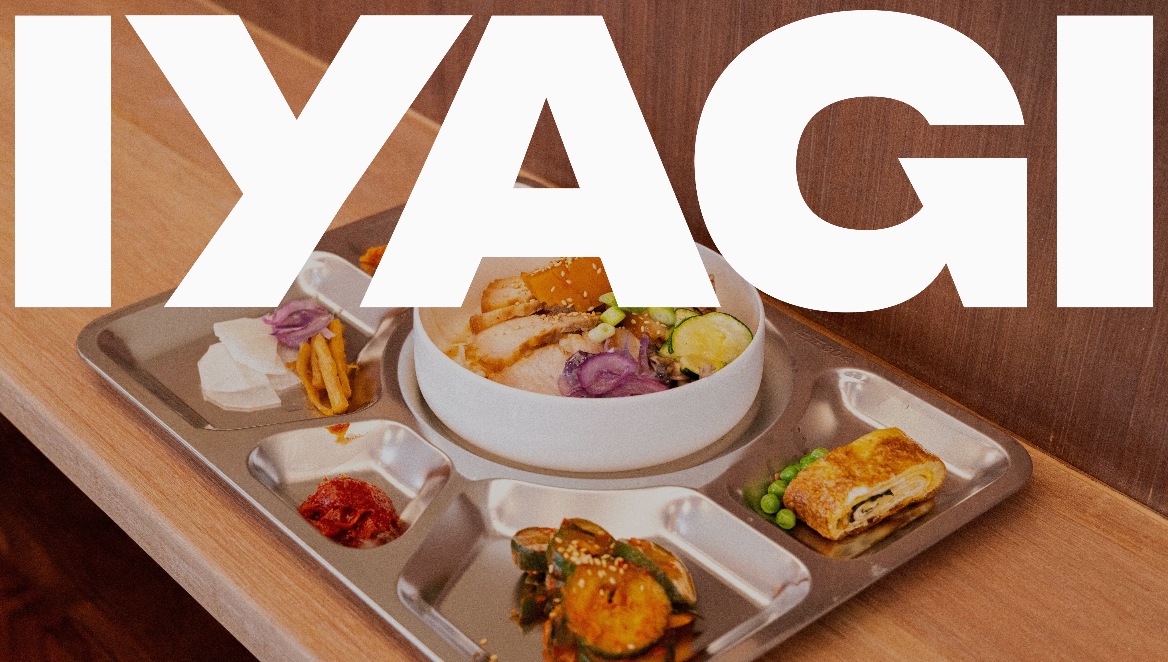 Tray of food with a bowl and various dishes on a wooden table, featuring the brand 'IYAGI'.
