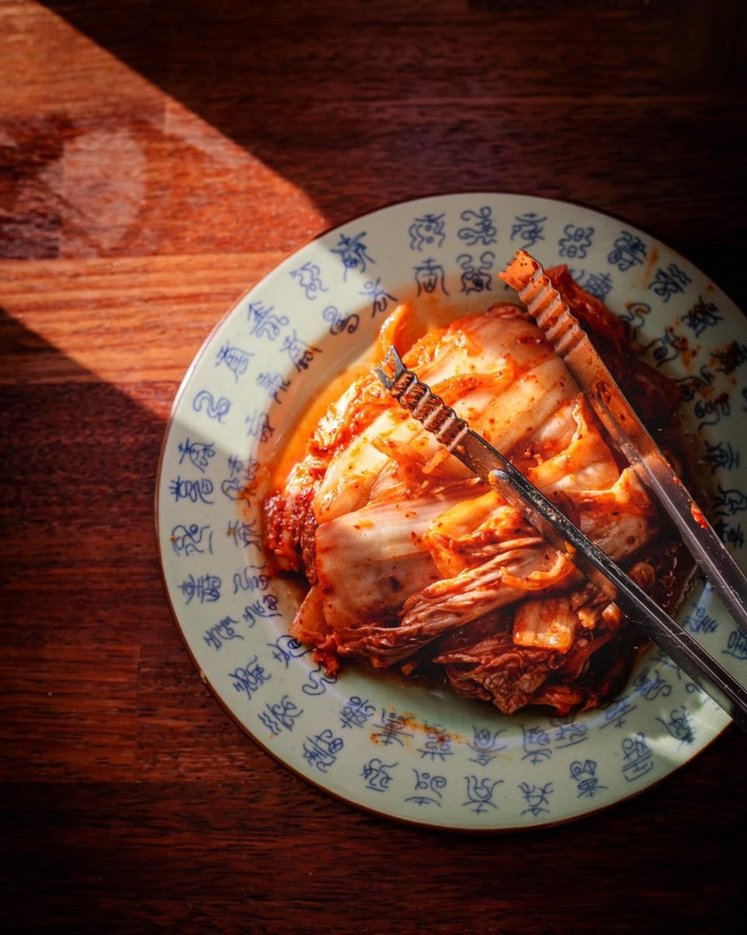 Kimchi on a plate with chopsticks on a wooden surface