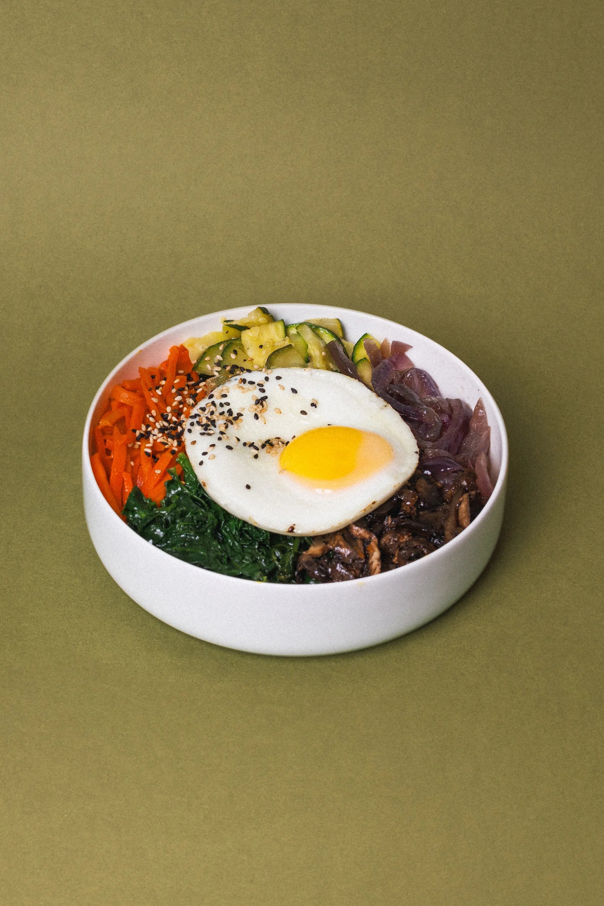 Photo of Korean Bibimbap rice dish served in a white bowl on green background. 